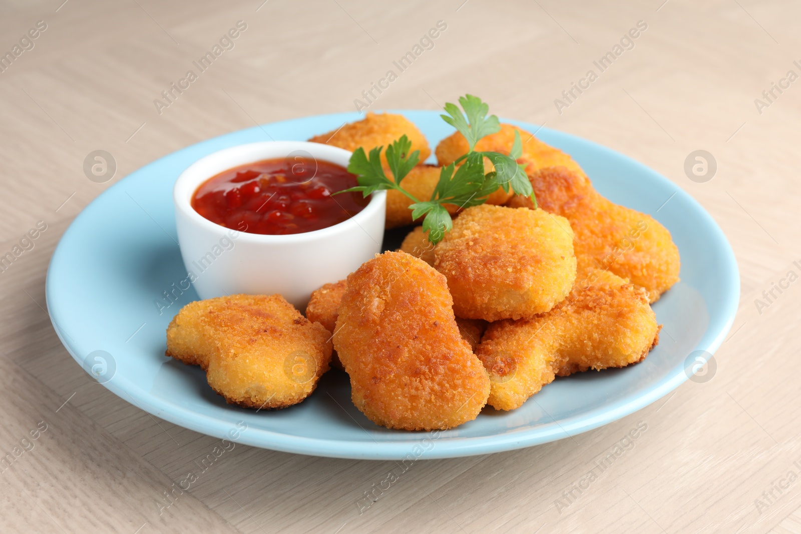 Photo of Tasty chicken nuggets with chili sauce and parsley on wooden table