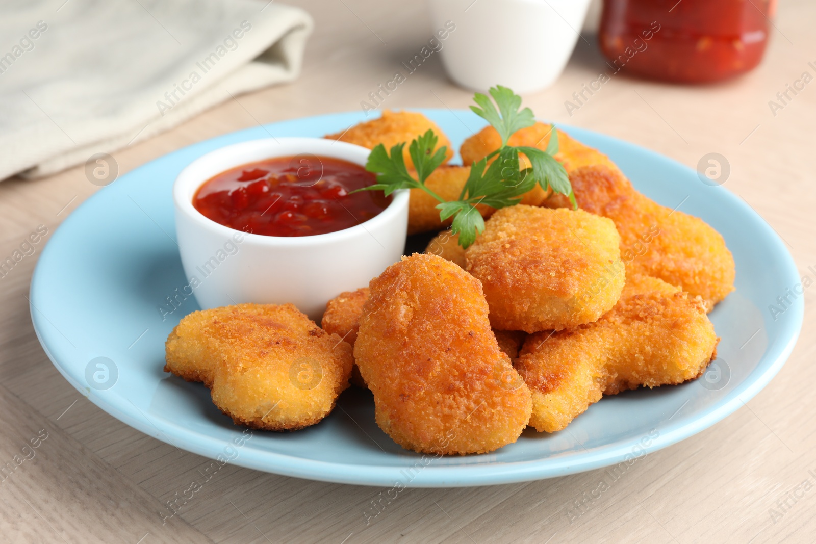 Photo of Tasty chicken nuggets with chili sauce and parsley on wooden table, closeup