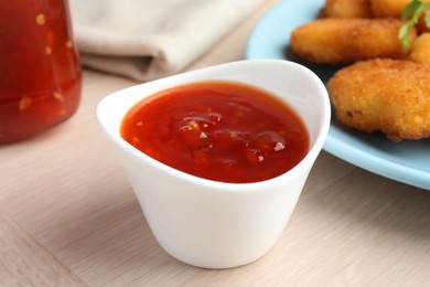 Photo of Spicy chili sauce in bowl on wooden table, closeup