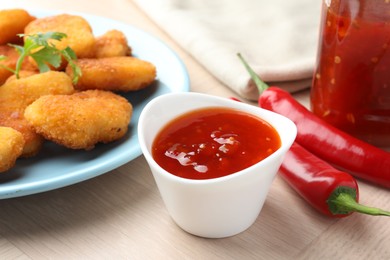 Photo of Spicy chili sauce in bowl and chicken nuggets on wooden table