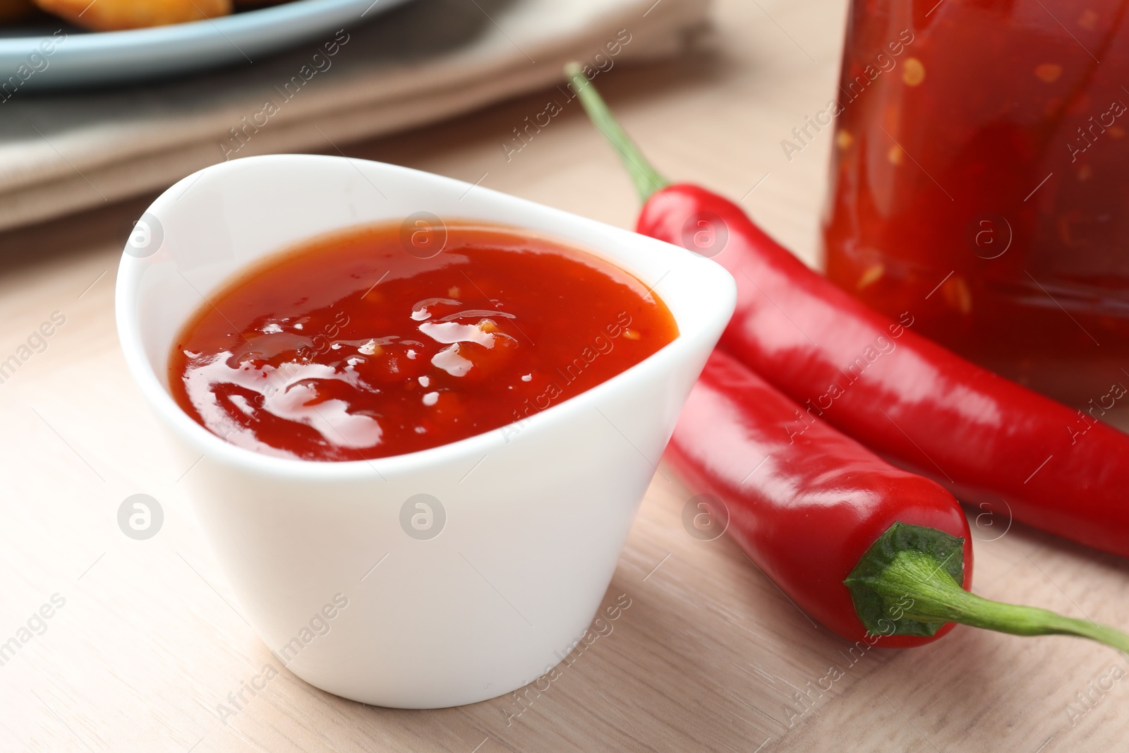 Photo of Spicy chili sauce in bowl on wooden table, closeup