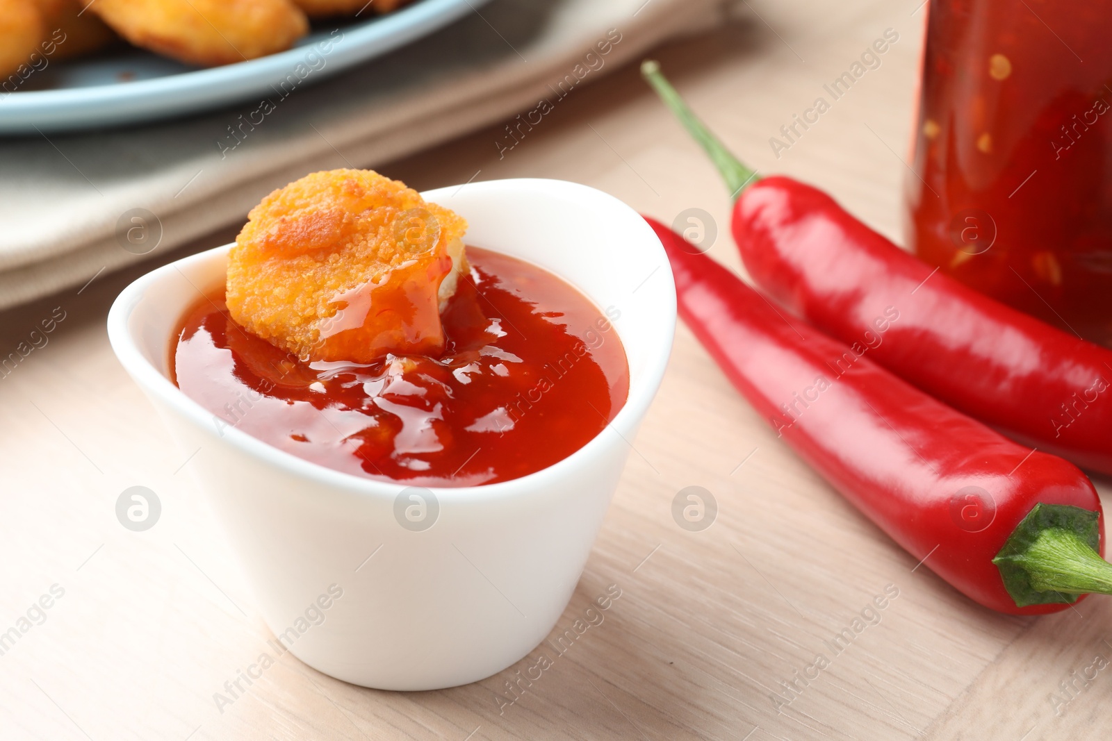 Photo of Chicken nugget into spicy chili sauce in bowl on wooden table, closeup