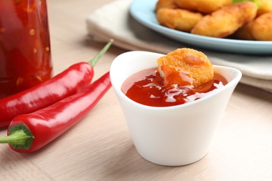 Photo of Chicken nugget into spicy chili sauce in bowl on wooden table, closeup