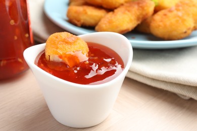 Photo of Chicken nugget into spicy chili sauce in bowl on wooden table, closeup