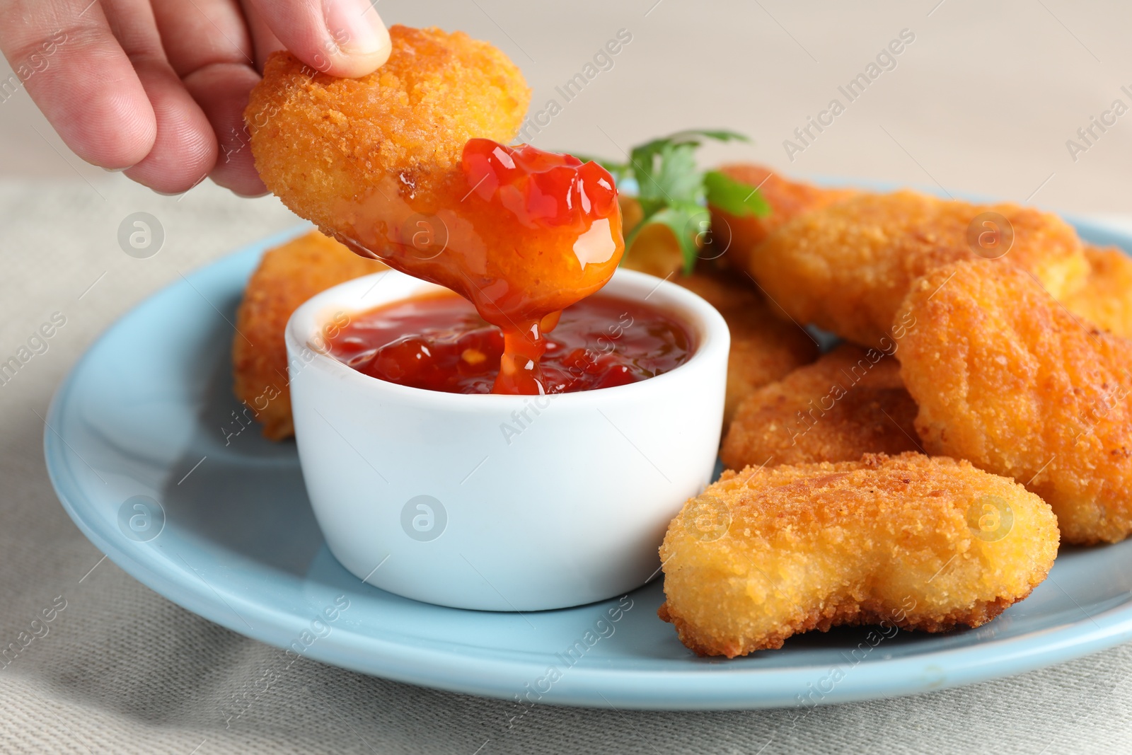 Photo of Woman dipping tasty chicken nugget into chili sauce at grey table, closeup