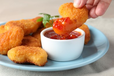 Photo of Woman dipping tasty chicken nugget into chili sauce at grey table, closeup