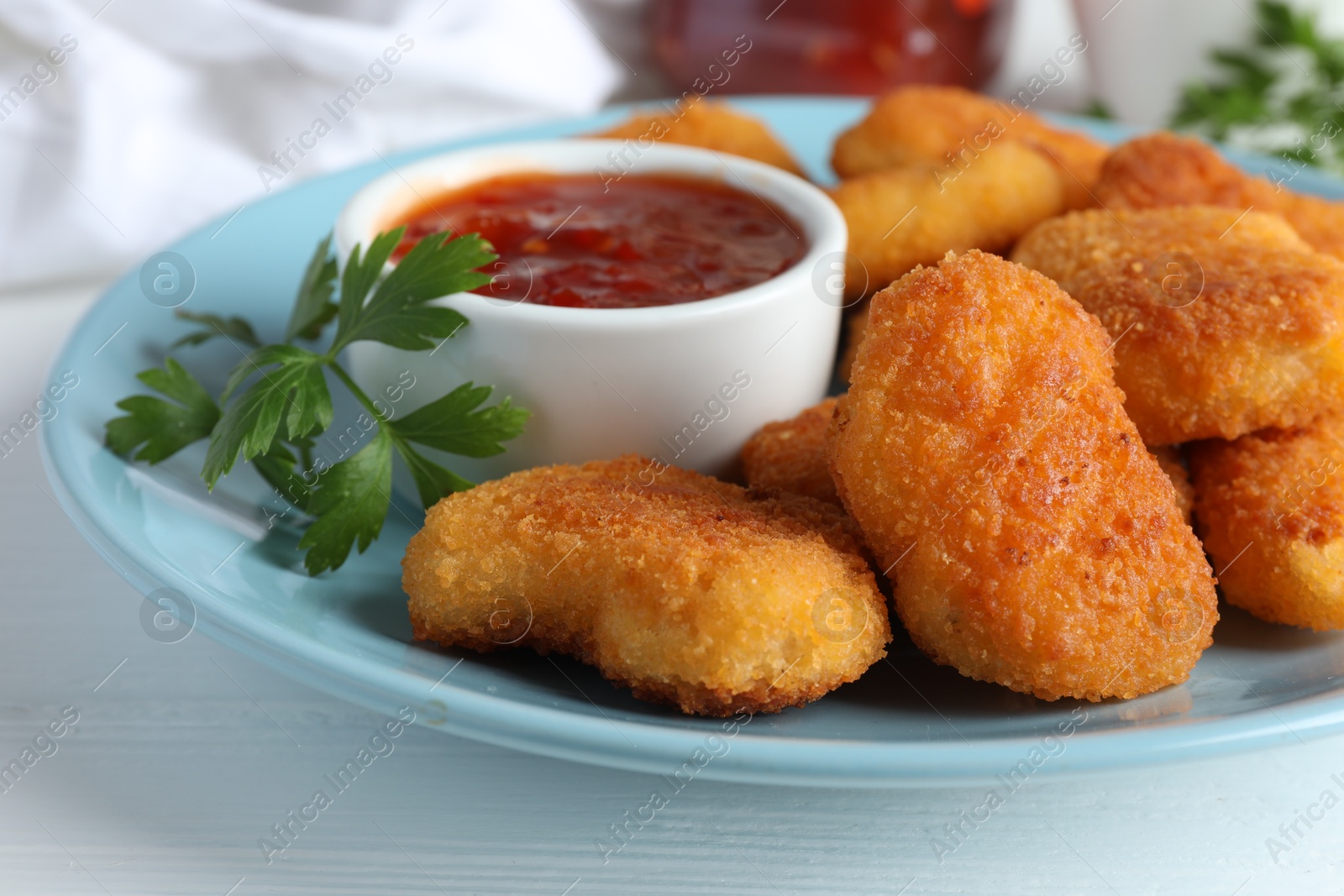 Photo of Tasty chicken nuggets with chili sauce and parsley on white table, closeup