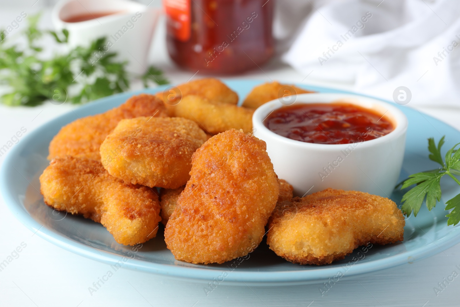 Photo of Tasty chicken nuggets with chili sauce and parsley on white table, closeup