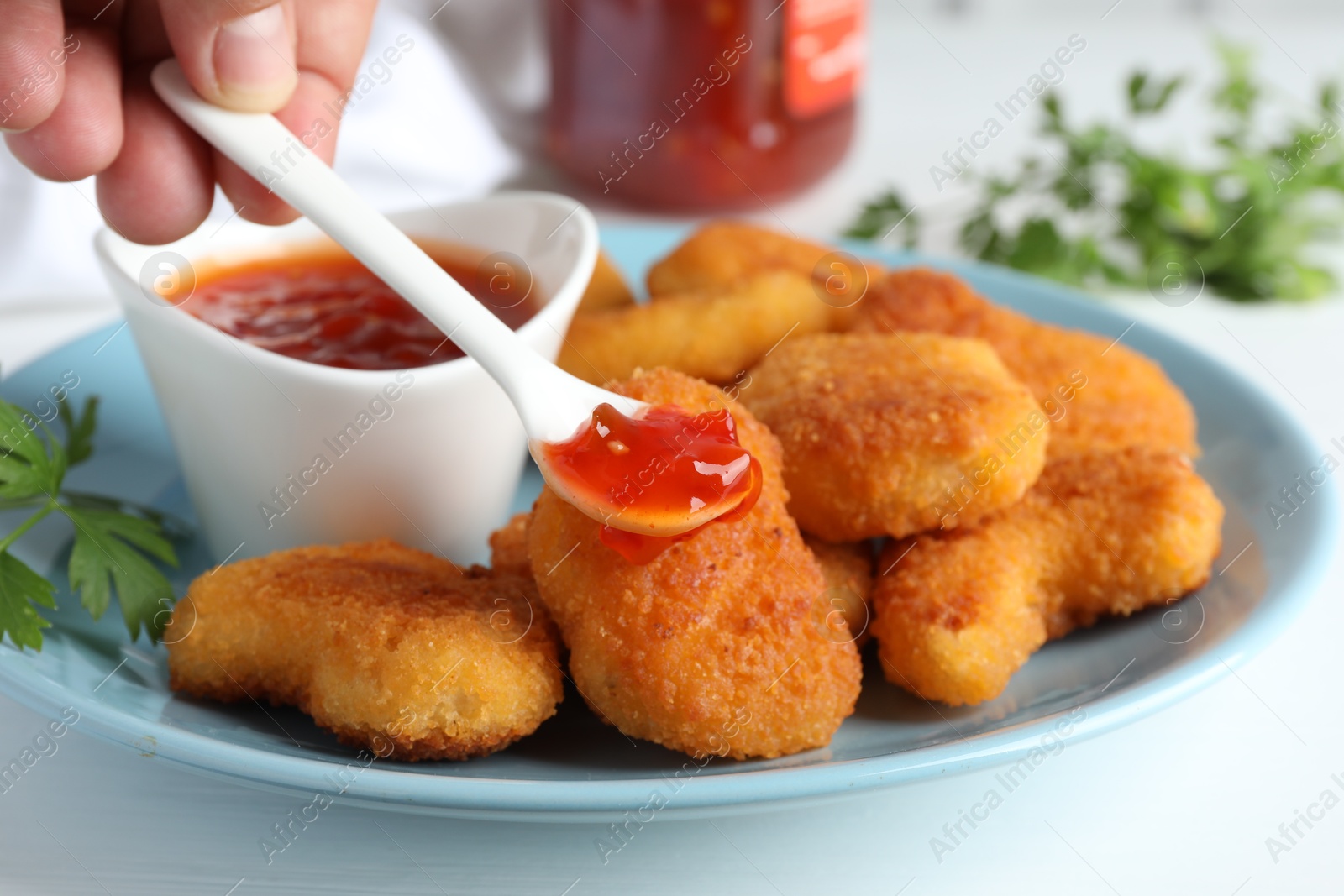 Photo of Woman eating tasty chicken nuggets with chili sauce at white table, closeup