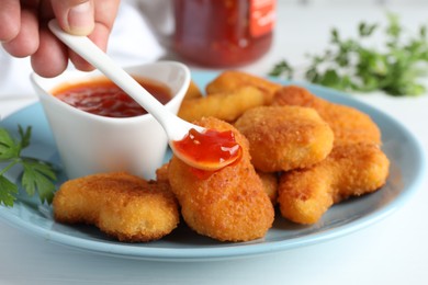 Photo of Woman eating tasty chicken nuggets with chili sauce at white table, closeup