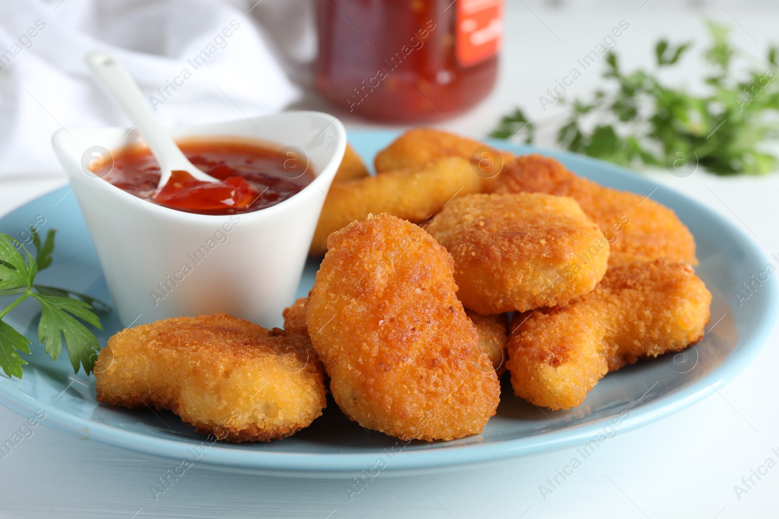 Photo of Tasty chicken nuggets with chili sauce and parsley on white table, closeup