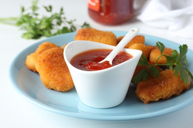 Photo of Tasty chicken nuggets with chili sauce and parsley on white table, closeup