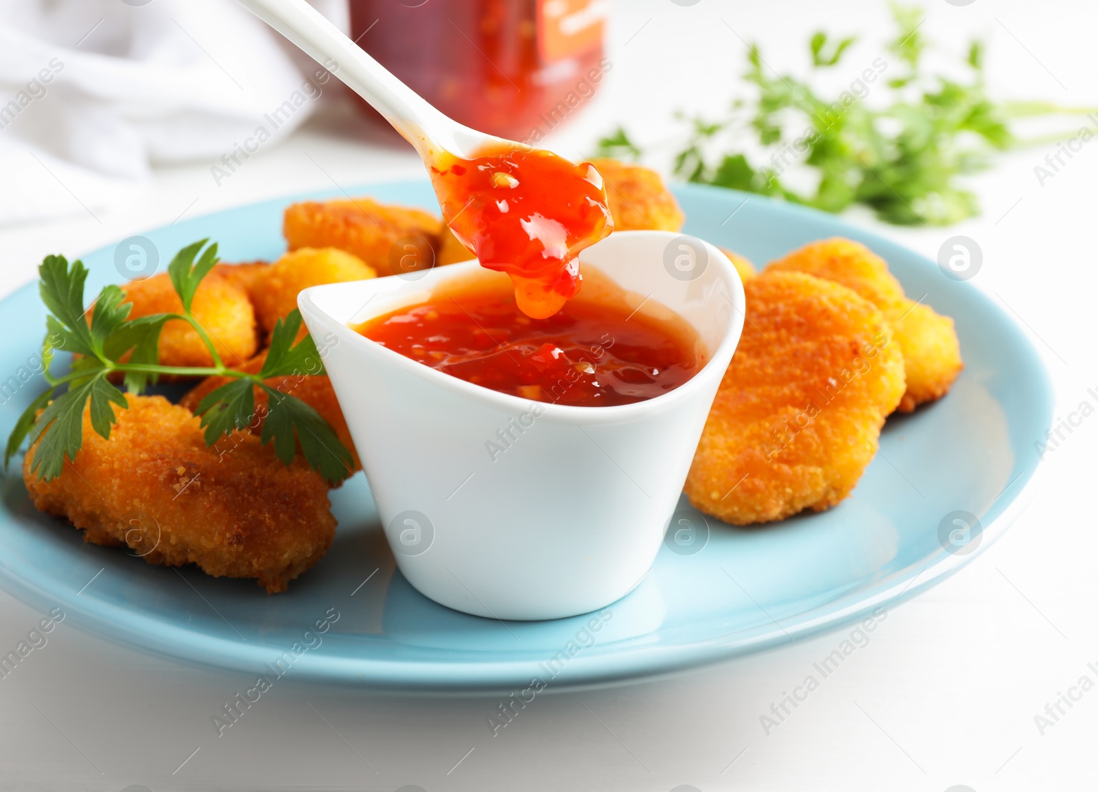 Photo of Eating tasty chicken nuggets with chili sauce at white table, closeup