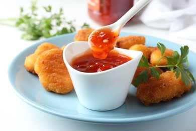 Photo of Eating tasty chicken nuggets with chili sauce at white table, closeup