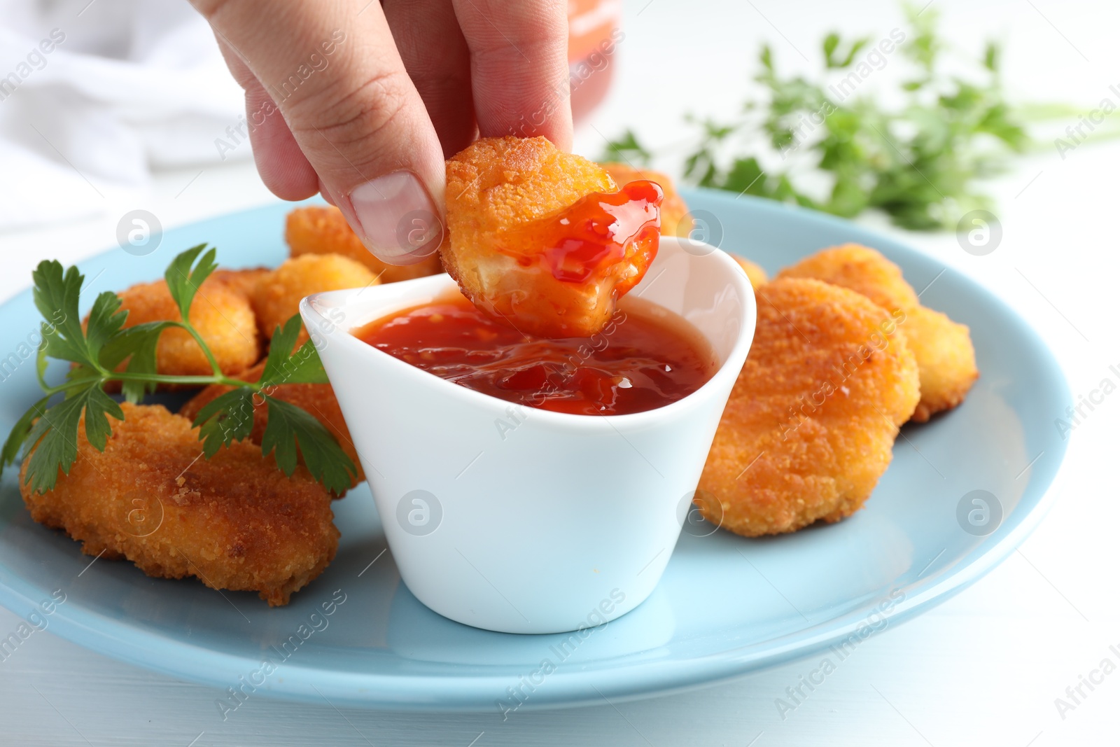 Photo of Woman dipping tasty chicken nugget into chili sauce at white table, closeup