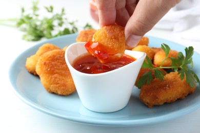 Photo of Woman dipping tasty chicken nugget into chili sauce at white table, closeup