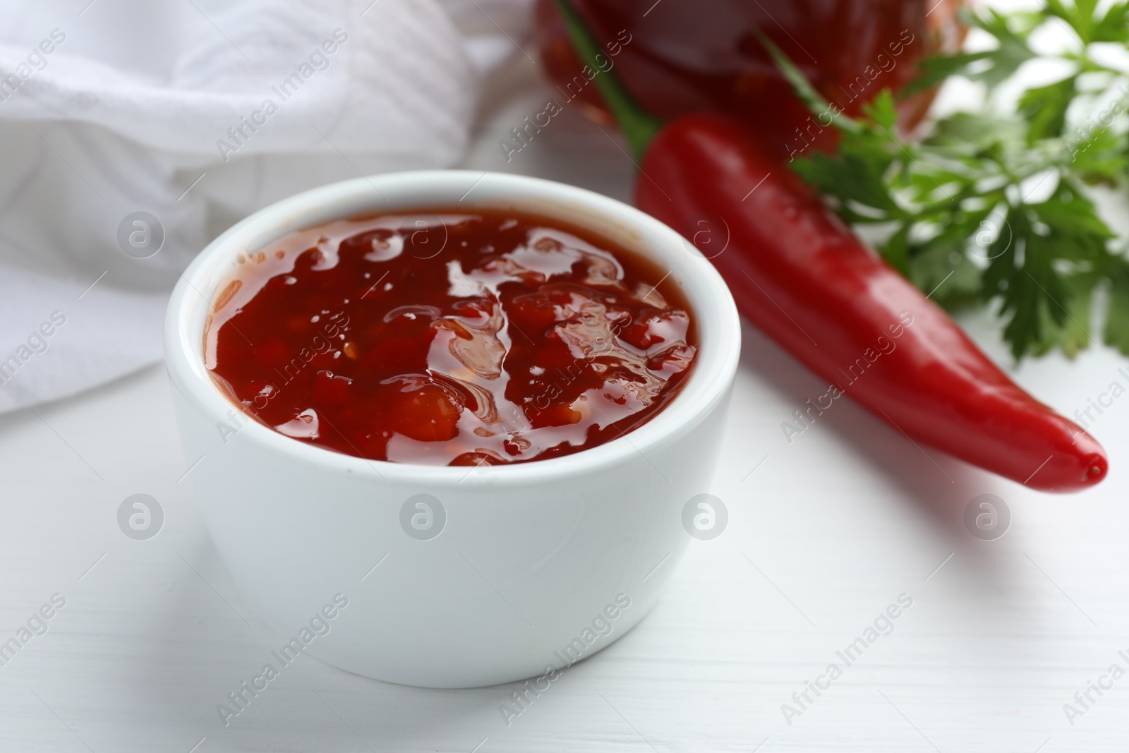 Photo of Spicy chili sauce in bowl on white wooden table, closeup