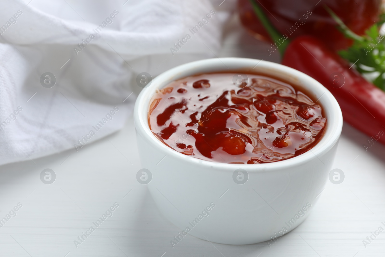 Photo of Spicy chili sauce in bowl on white wooden table, closeup