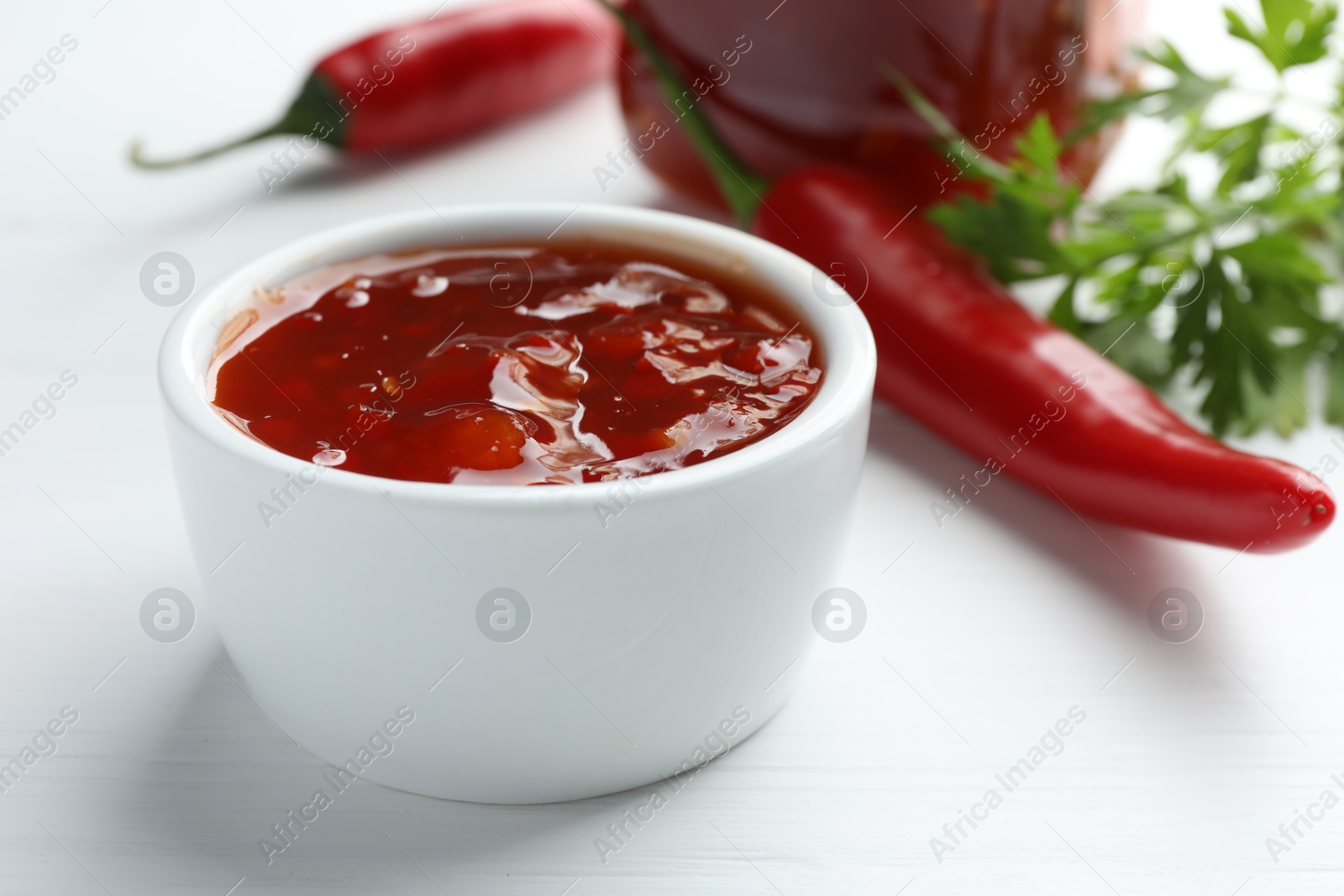 Photo of Spicy chili sauce in bowl on white wooden table, closeup