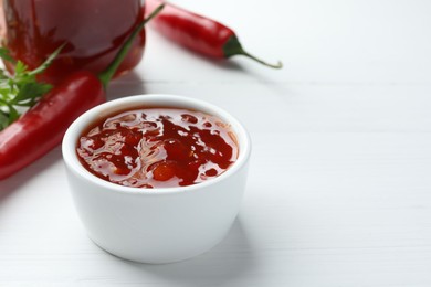 Photo of Spicy chili sauce in bowl on white wooden table, space for text