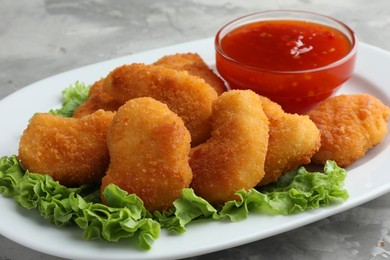 Photo of Tasty chicken nuggets with chili sauce and lettuce on grey textured table, closeup