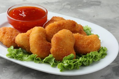 Photo of Tasty chicken nuggets with chili sauce and lettuce on grey textured table, closeup