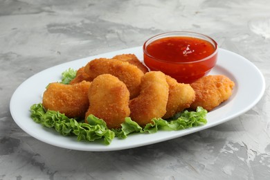 Photo of Tasty chicken nuggets with chili sauce and lettuce on grey textured table