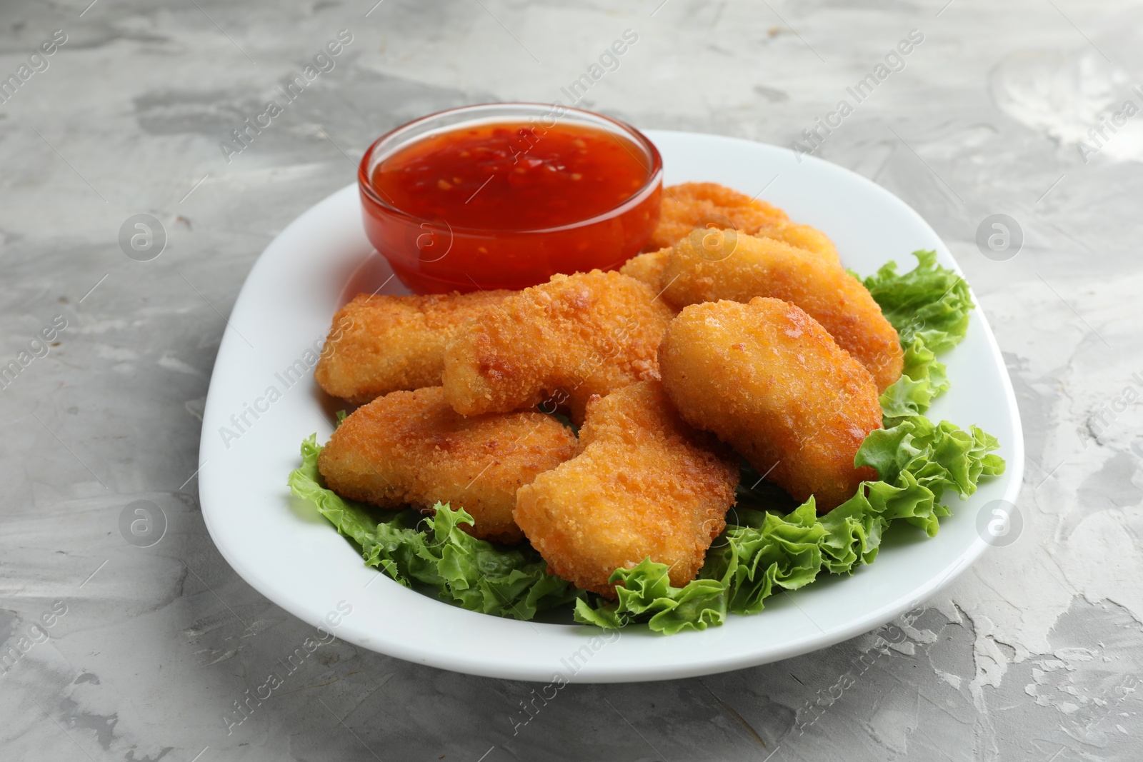 Photo of Tasty chicken nuggets with chili sauce and lettuce on grey textured table