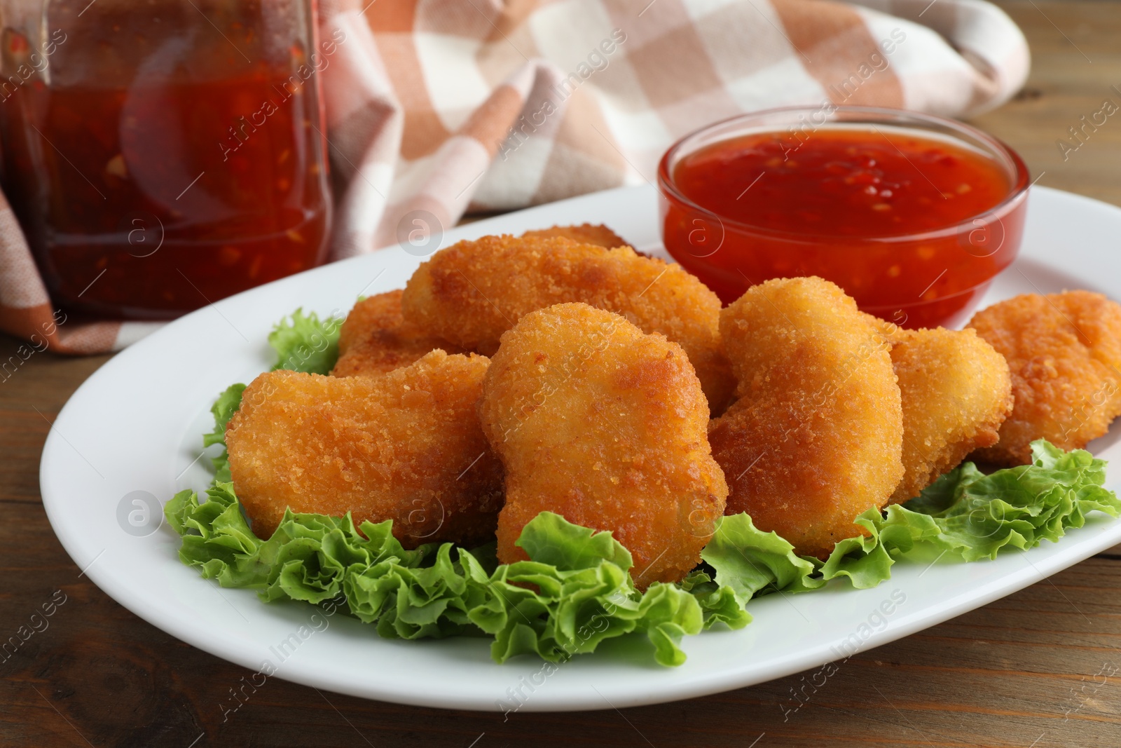 Photo of Tasty chicken nuggets with chili sauce and lettuce on wooden table, closeup