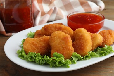 Photo of Tasty chicken nuggets with chili sauce and lettuce on wooden table, closeup