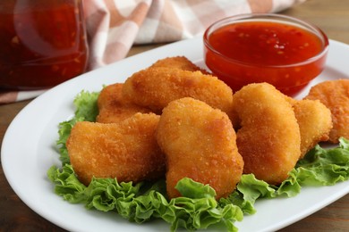 Photo of Tasty chicken nuggets with chili sauce and lettuce on table, closeup