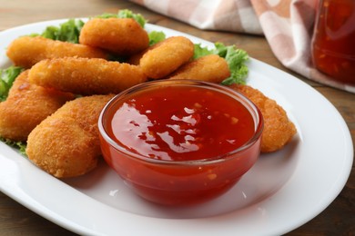 Photo of Tasty chicken nuggets with chili sauce and lettuce on table, closeup