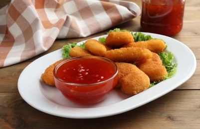 Photo of Tasty chicken nuggets with chili sauce and lettuce on wooden table