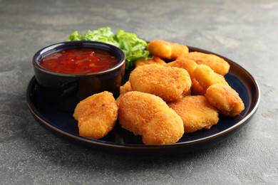 Photo of Tasty chicken nuggets with chili sauce on grey table