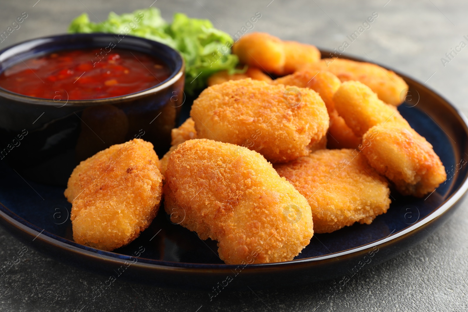 Photo of Tasty chicken nuggets with chili sauce on grey table, closeup