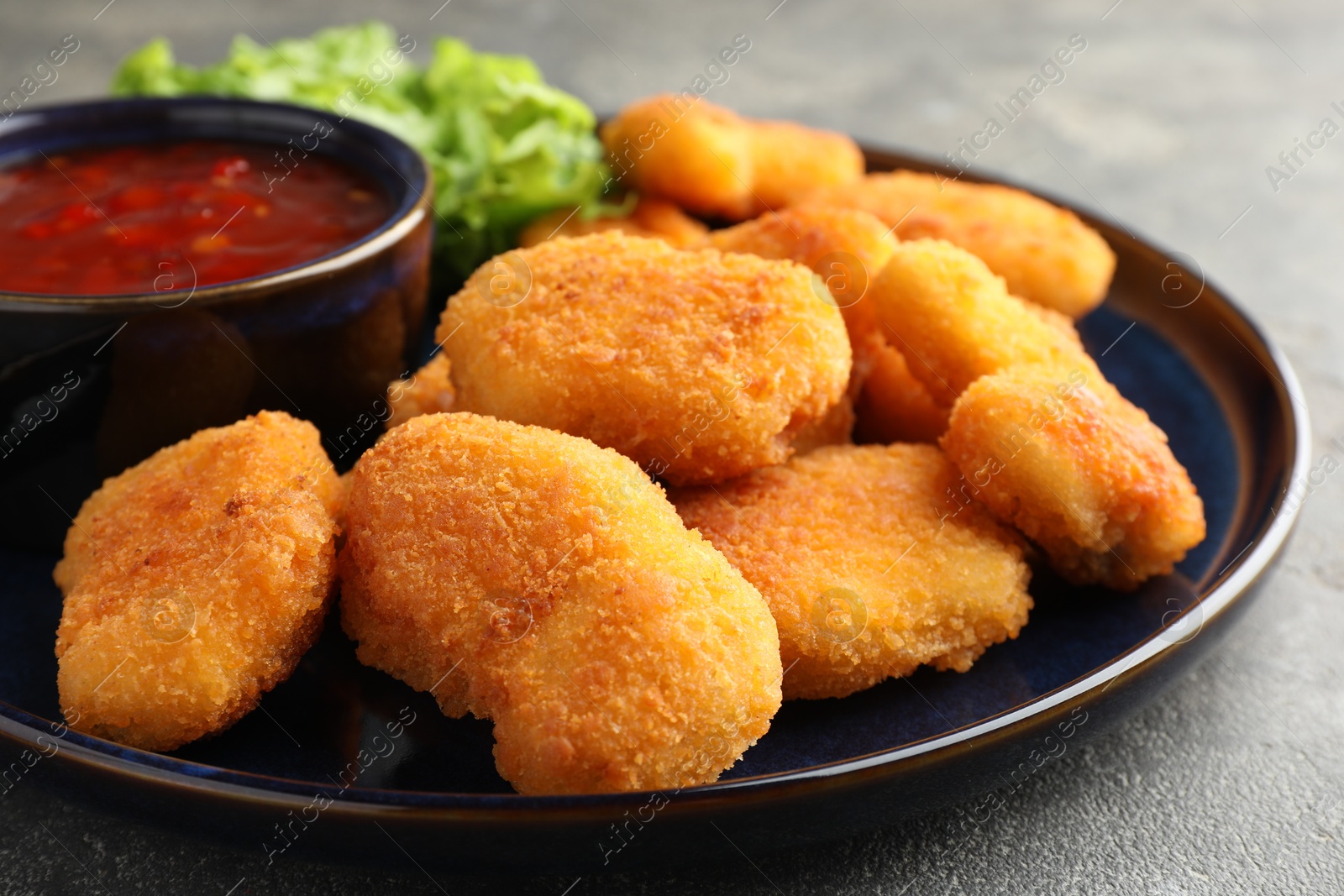 Photo of Tasty chicken nuggets with chili sauce on grey table, closeup