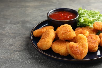 Photo of Tasty chicken nuggets with chili sauce on grey table, closeup