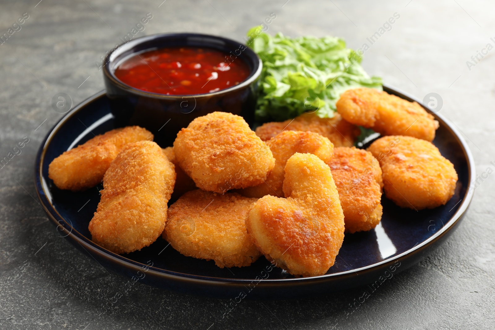 Photo of Tasty chicken nuggets with chili sauce on grey table