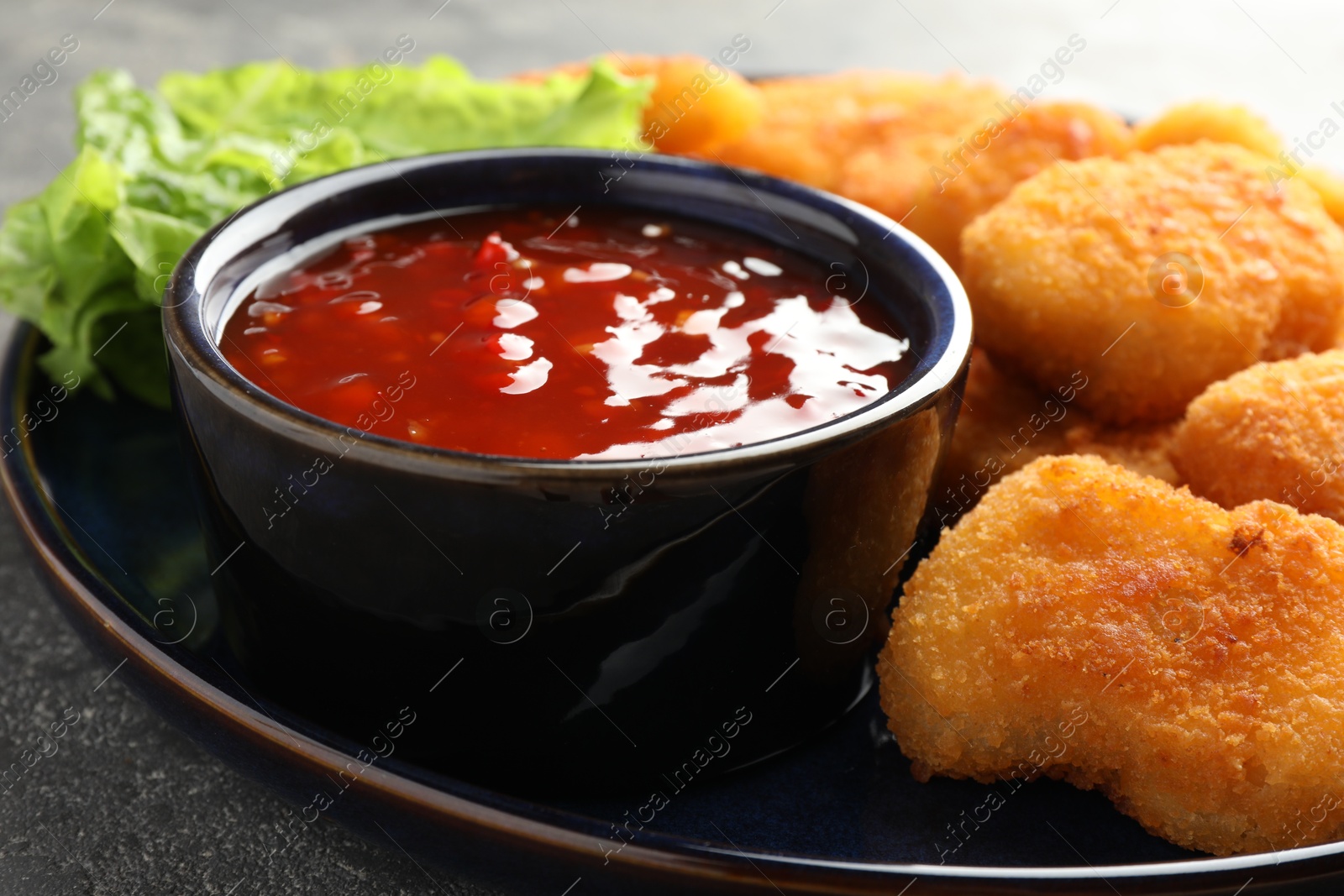 Photo of Chili sauce with tasty chicken nuggets on grey table, closeup