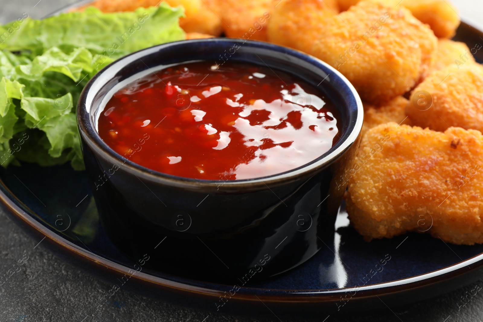 Photo of Chili sauce with tasty chicken nuggets on grey table, closeup