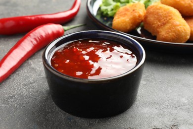 Photo of Spicy chili sauce in bowl on grey textured table, closeup