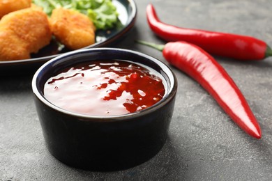 Photo of Spicy chili sauce in bowl on grey textured table, closeup