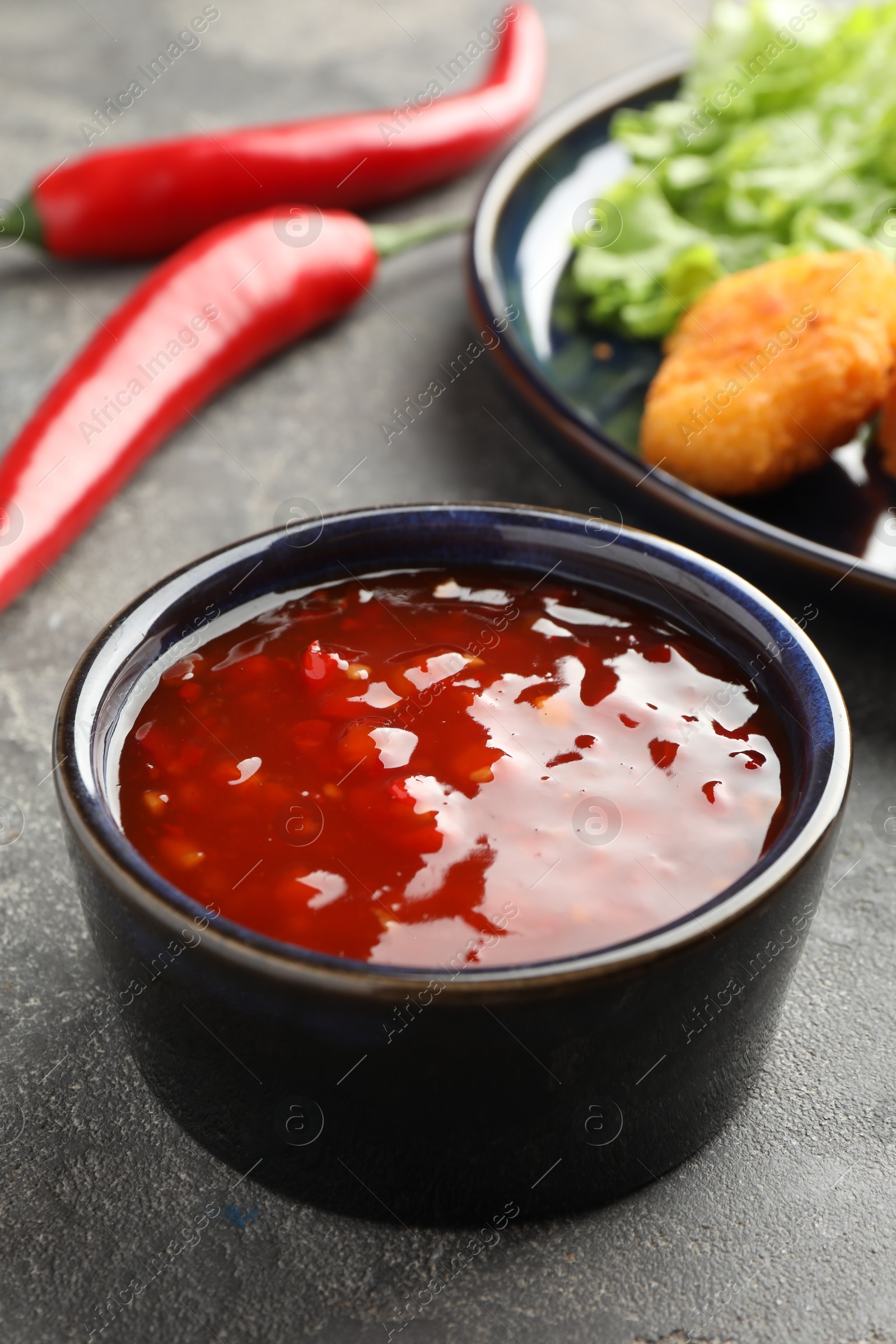 Photo of Spicy chili sauce in bowl on grey textured table, closeup