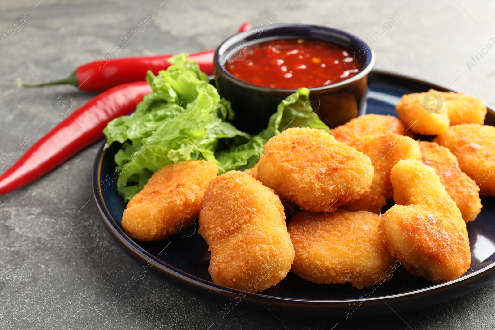 Photo of Tasty chicken nuggets with chili sauce and lettuce on grey table, closeup