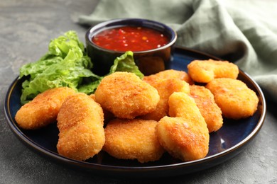 Photo of Tasty chicken nuggets with chili sauce and lettuce on grey table, closeup