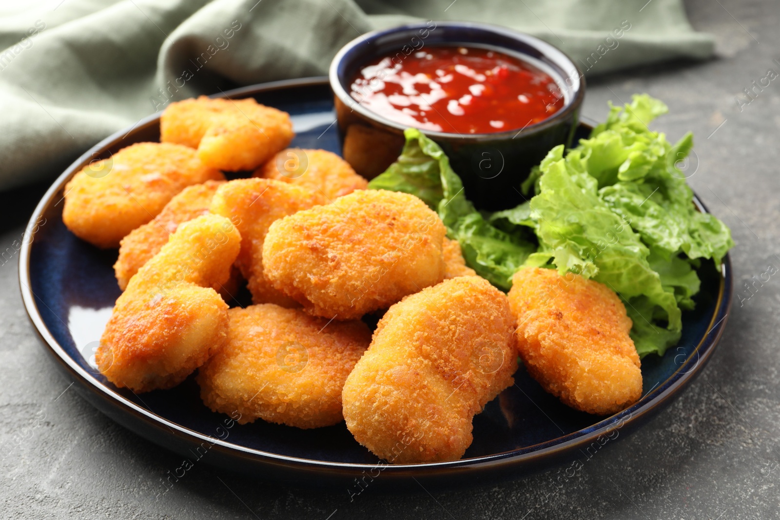 Photo of Tasty chicken nuggets with chili sauce and lettuce on grey table, closeup