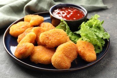 Photo of Tasty chicken nuggets with chili sauce and lettuce on grey table, closeup