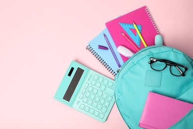 Backpack with different school stationery on pink background, flat lay. Space for text