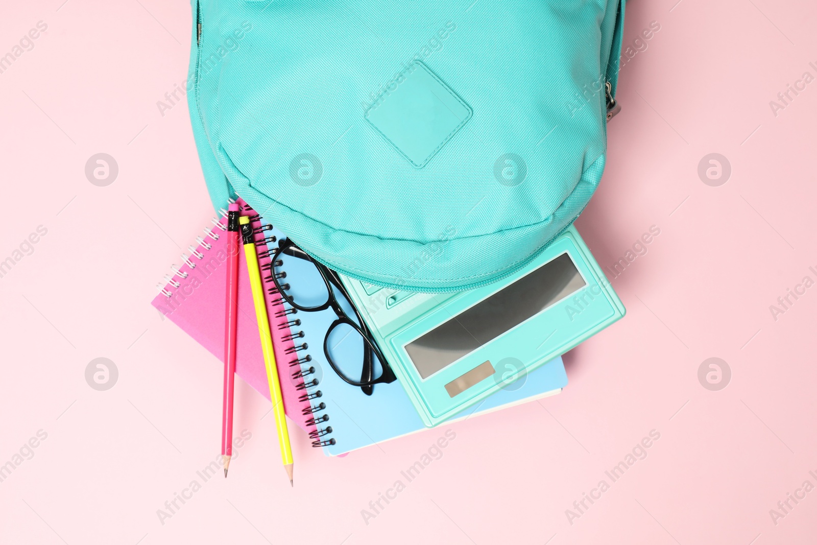 Photo of Backpack with different school stationery on pink background, top view