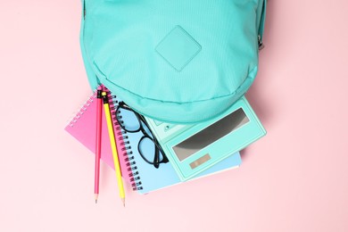 Photo of Backpack with different school stationery on pink background, top view